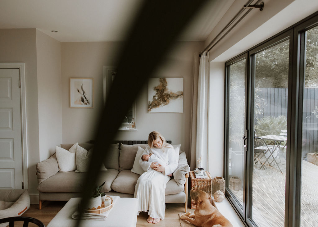 Mother nursing newborn on sofa during intimate in-home newborn photography session