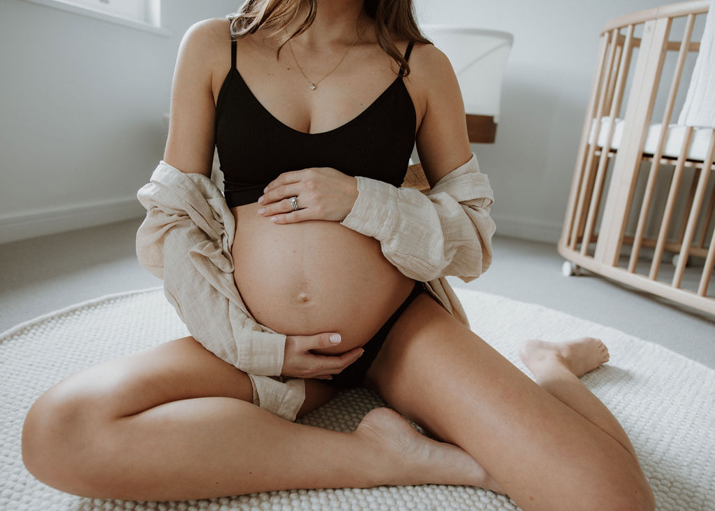 Pregnant mother gently touching her belly in a cosy, light-filled nursery during a luxury in-home maternity photography session in London.