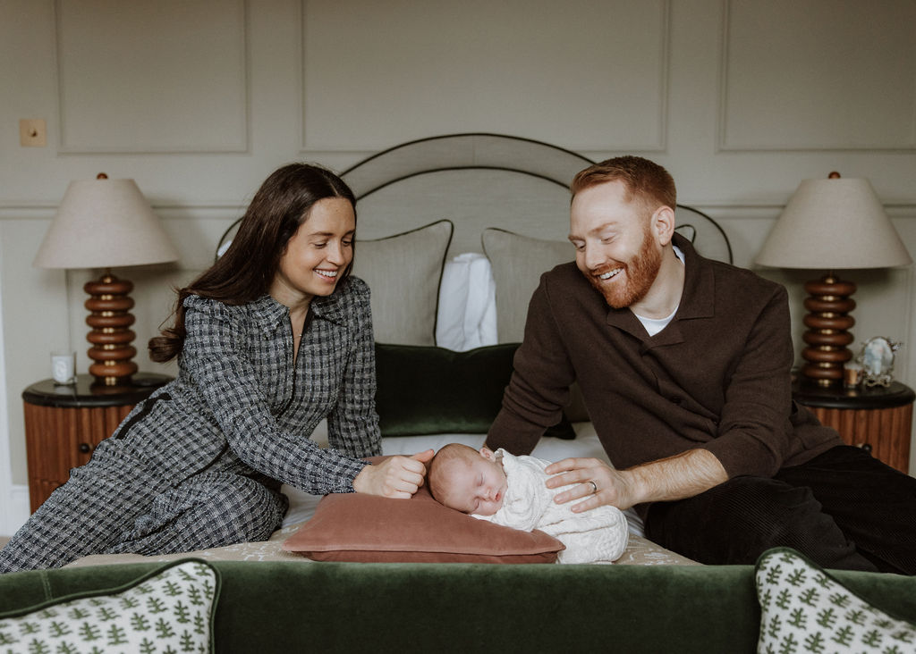 Parents gazing lovingly at their newborn during in-home photography session in master bedroom