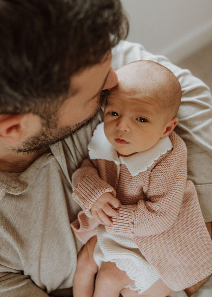 Father embracing their newborn daughter, Sienna, in their Surrey home during a newborn photoshoot.